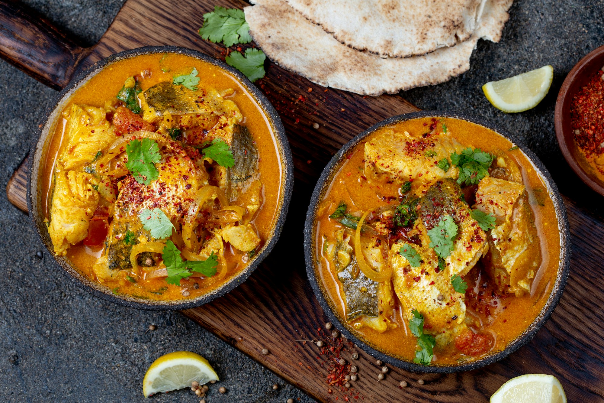 INDIAN FOOD. Traditional KERALA FISH CURRY with naan bread, gray plate, black background