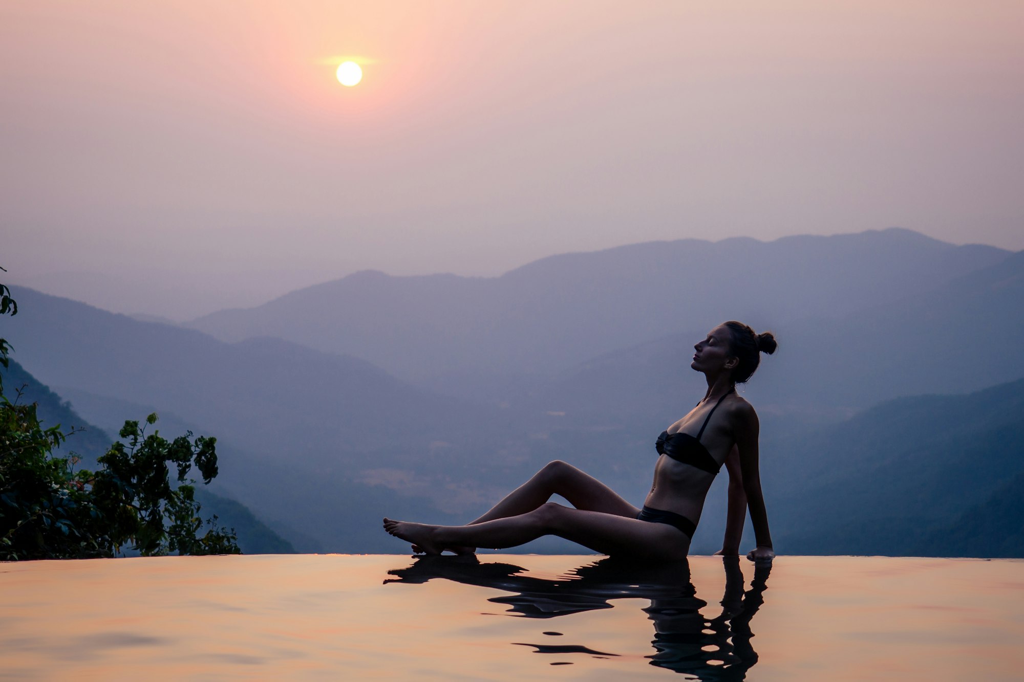 Young woman relaxing in infinity swimming pool looking at view romantic sunset